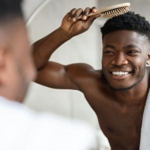 Cheerful Black Guy Brushing Short Hair With Hairbrush In Bathroom