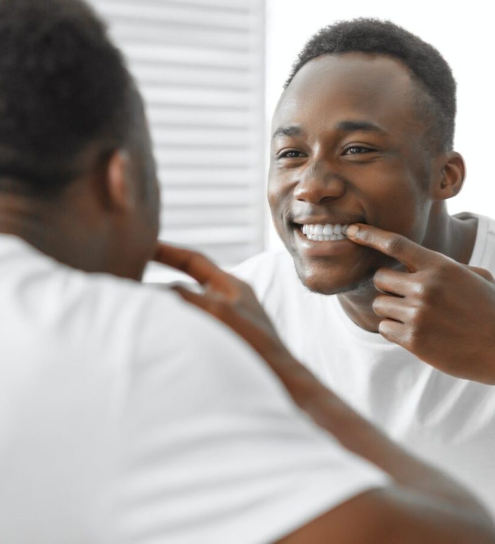 African Man Checking Teeth Smiling To Mirror Standing In Bathroom