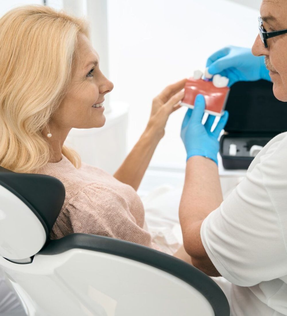 Dentist holding model of teeth with dental implant